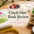 Cinch Diet Book Review featured image with the Cinch book, berries, yogurt, spinach, almonds, eggs, and a measuring tape on a warm wooden table.