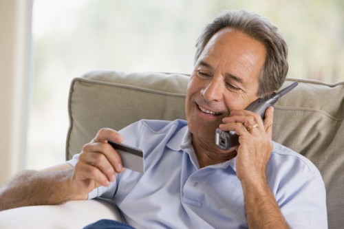 Man indoors using telephone and looking at credit card smiling