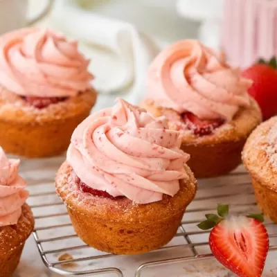 Strawberry cupcakes with pink strawberry frosting, baked strawberry slices, and fresh strawberries on a cooling rack