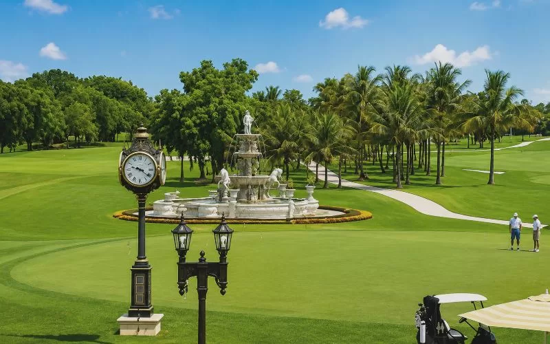 Golf course view with a fountain, palm trees, clock, and golfers at Trump National Doral Miami.