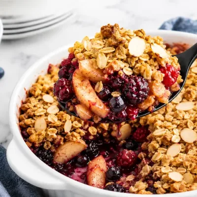 Warm apple berry crumble with a golden oat and almond topping served from a white baking dish