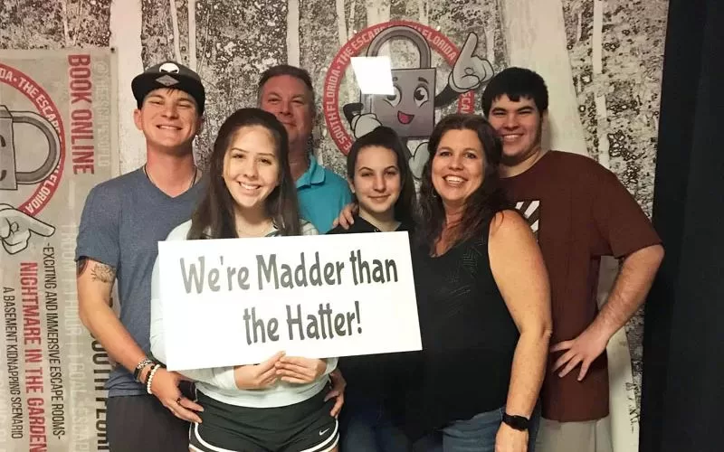 Family group holding a We’re Madder Than the Hatter sign after completing an Alice in Wonderland themed escape room.