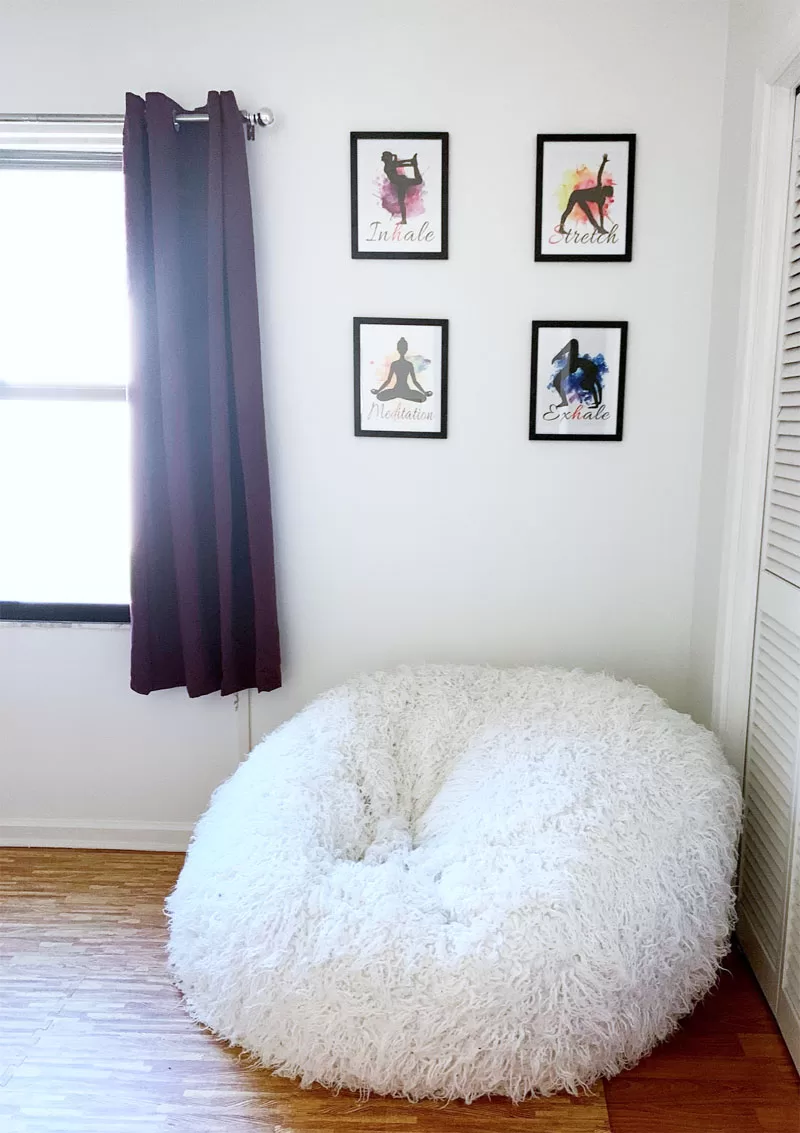 Four framed yoga prints displayed above an oversized white bean bag chair in a workout room corner.