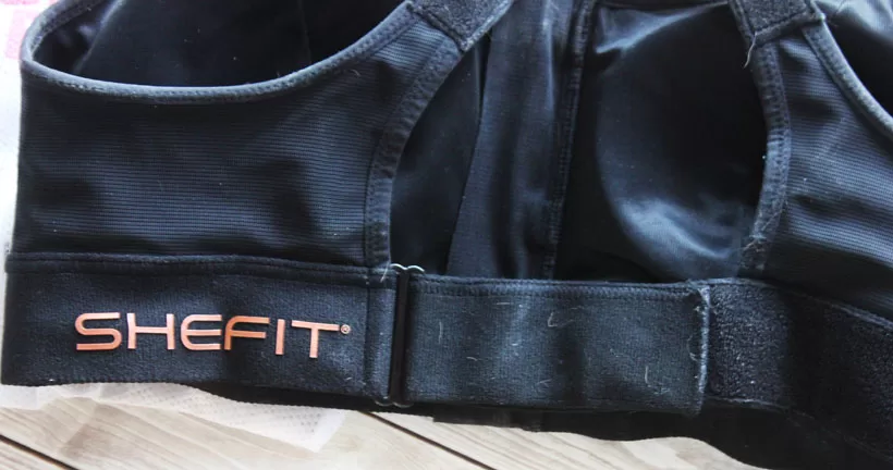 Interior view of a black SHEFIT Ultimate Sports Bra showing the wide adjustable rib band and Velcro closure.