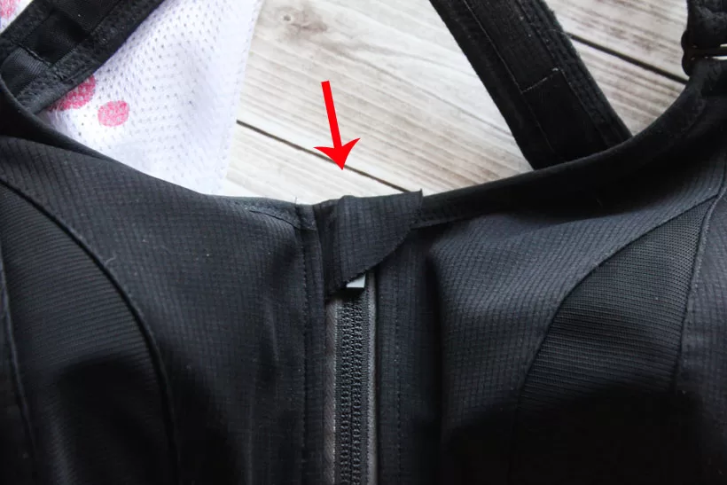 Close-up of the front zipper and hook closure on a black SHEFIT Ultimate Sports Bra, highlighted with a red arrow.