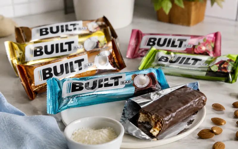 Original-style BUILT Bars arranged on a kitchen counter with one chocolate protein bar partially unwrapped.