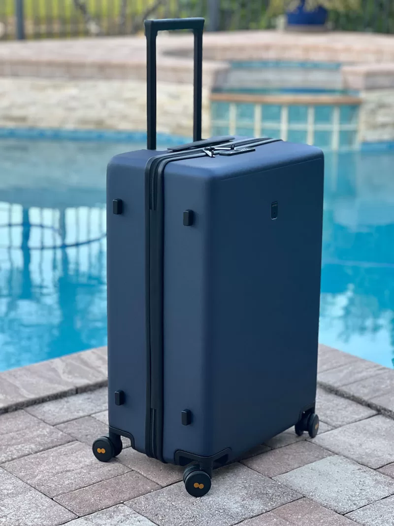 Navy LEVEL8 hard shell suitcase with spinner wheels and an extended handle standing beside a swimming pool.