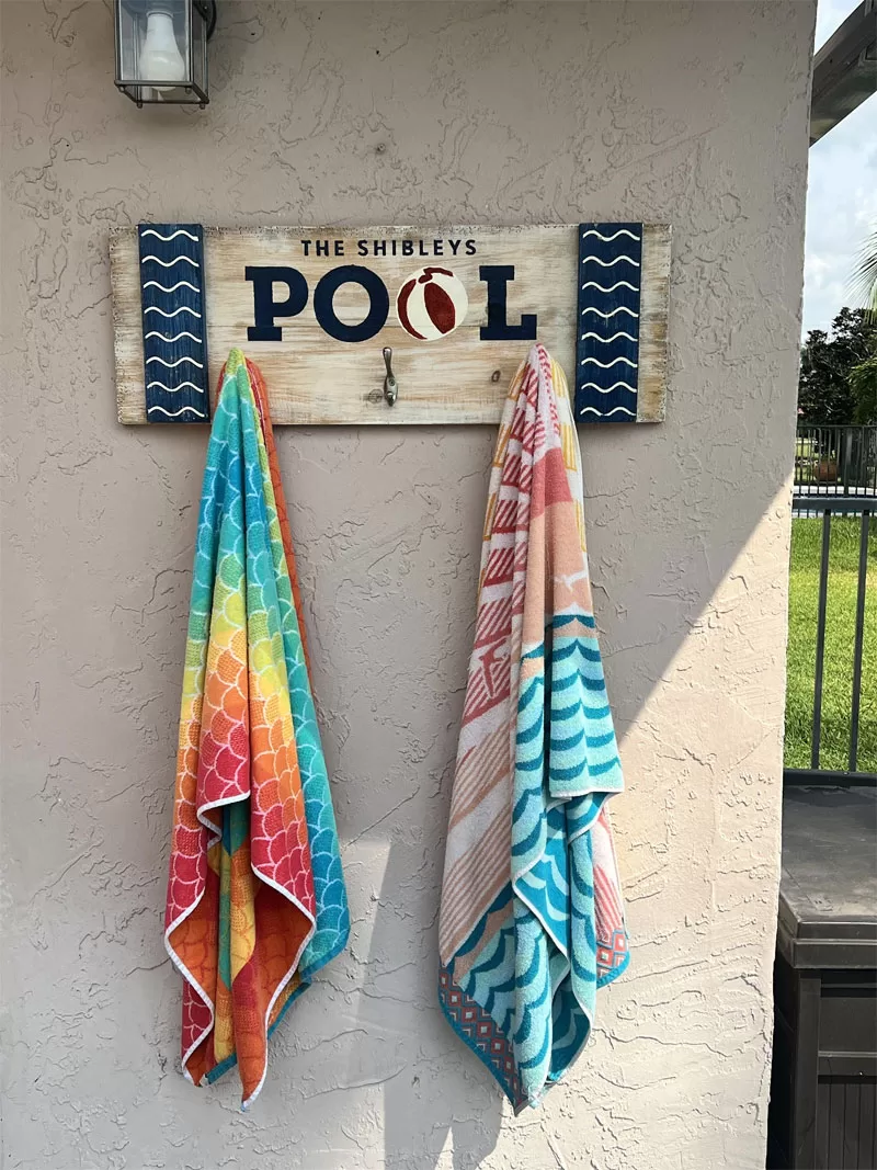 Custom pool towel rack hanging on a patio wall with colorful beach towels.