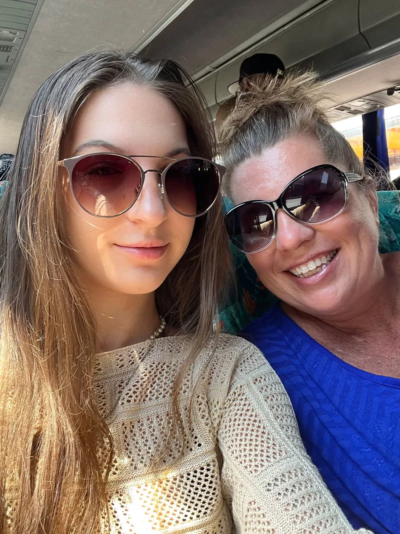 Mother and daughter wearing sunglasses while riding a bus during a cruise vacation.
