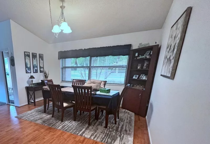 Dining room before the update with dark cherry furniture, older chandelier, dark window treatment, and brown corner cabinet.