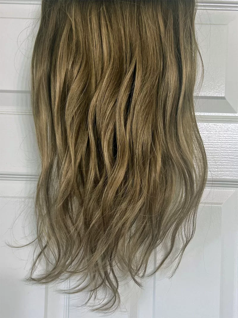 Caramel balayage clip-in hair extensions hanging against a white door before being styled.