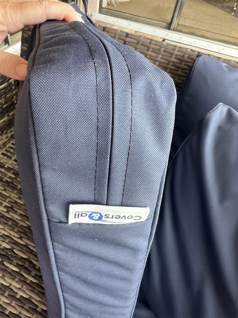 Close-up of a navy Covers & All patio cushion cover showing the zipper, piping, fabric texture, and product label