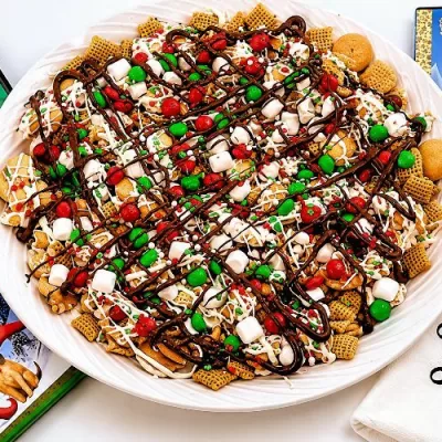 Holiday Sweet Maple Chex Mix recipe served on a white platter with chocolate drizzle, marshmallows, festive candies, and classic Christmas movie DVDs nearby.