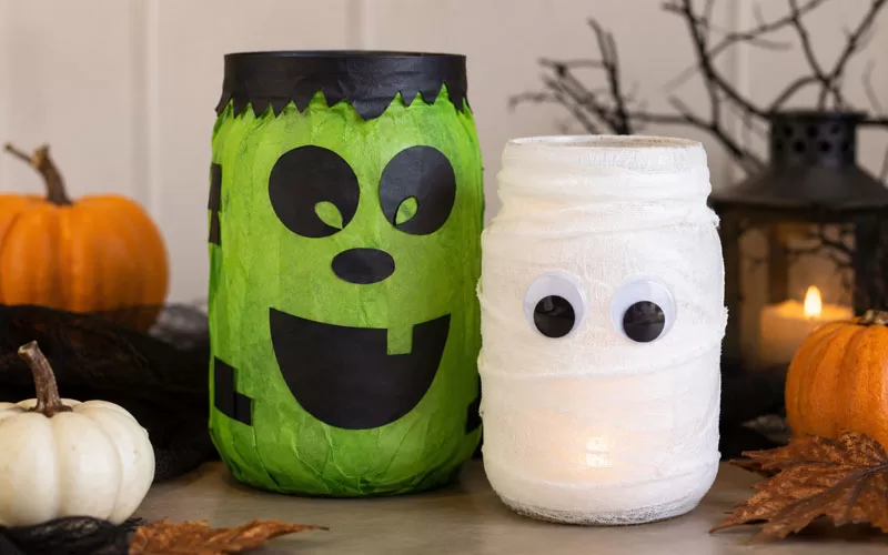 Frankenstein and mummy mason jar lanterns glowing beside pumpkins and Halloween decorations