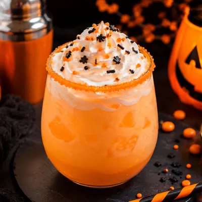 Creamy orange Halloween Screamsicle cocktail topped with whipped cream and black and orange sprinkles surrounded by pumpkins and spooky Halloween decor.