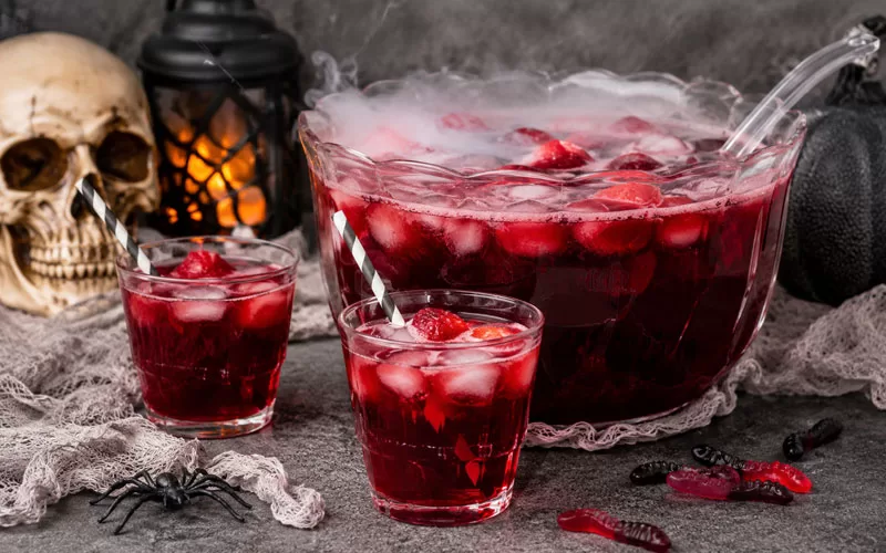 Halloween Blood Punch served in a spooky punch bowl with fog effects, red drinks, skull decor, gummy worms, and Halloween party decorations.