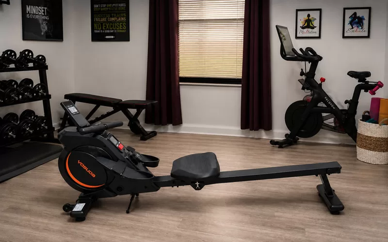 osuda RM2 rowing machine review showing a compact rowing machine in a home gym workout room with fitness equipment and motivational wall decor.